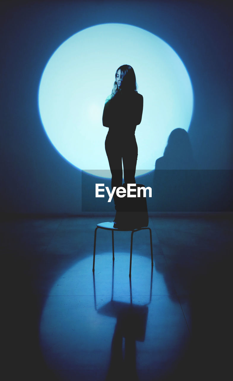 Young woman standing on chair against spotlight