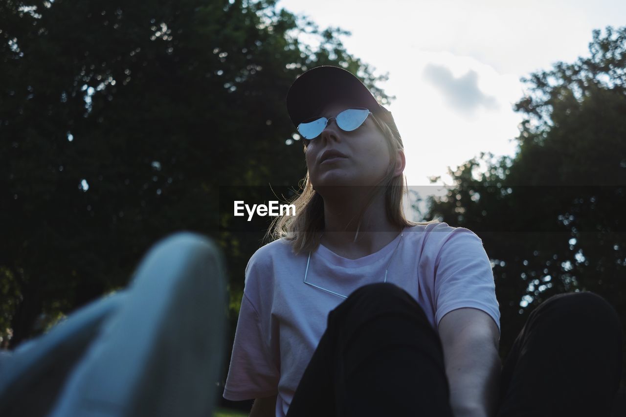 CLOSE-UP OF WOMAN IN SUNGLASSES AGAINST TREES