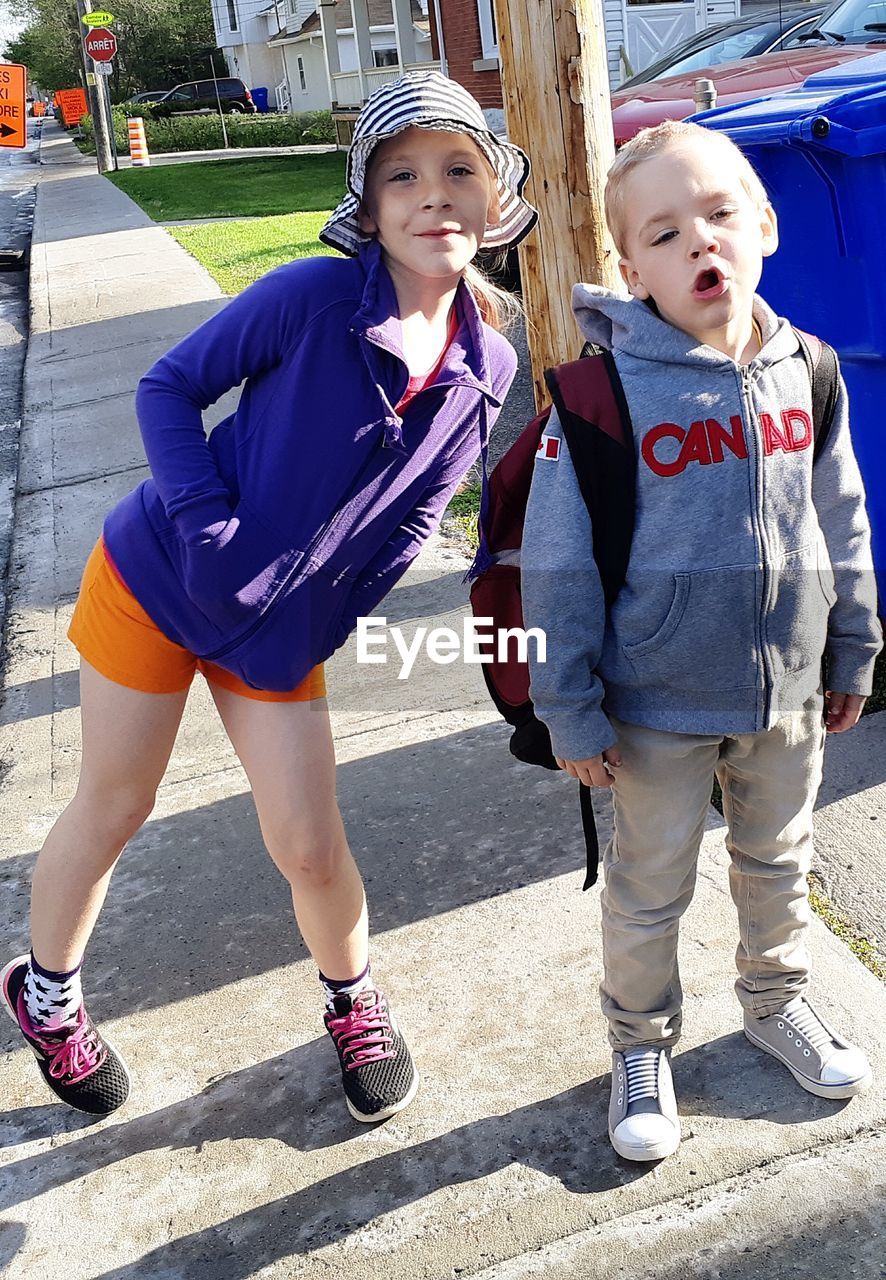 Portrait of siblings standing on sidewalk in city