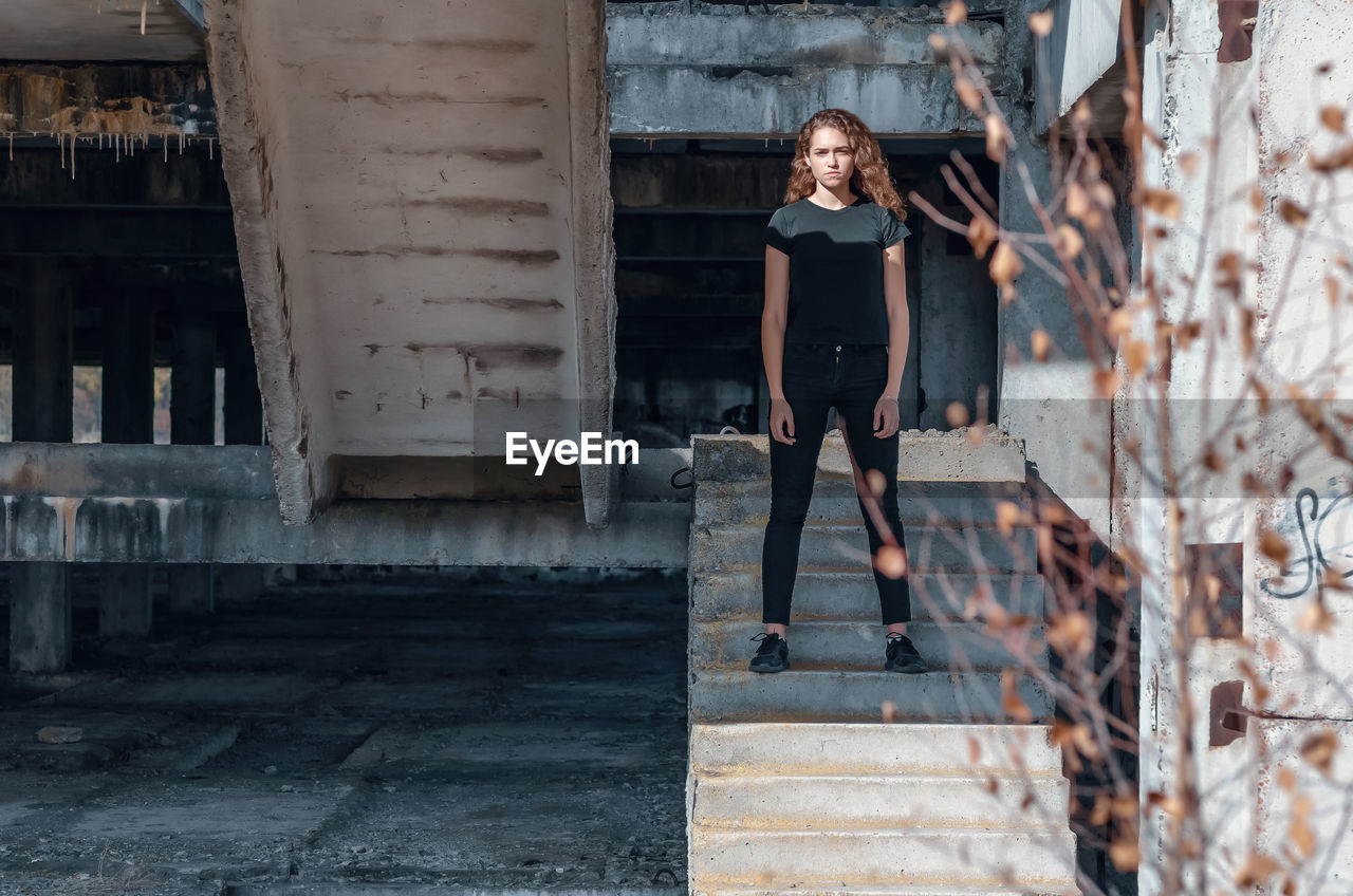 Cute teenage girl with curly hair standing on stairs. abandoned building, unfinished construction.