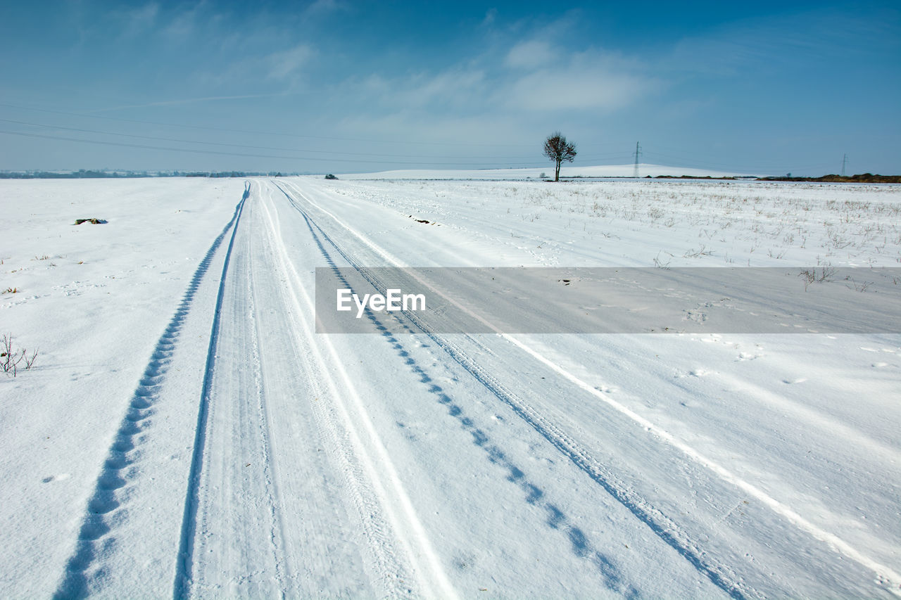 Road covered with snow, wheel tracks, horizon and blue sky