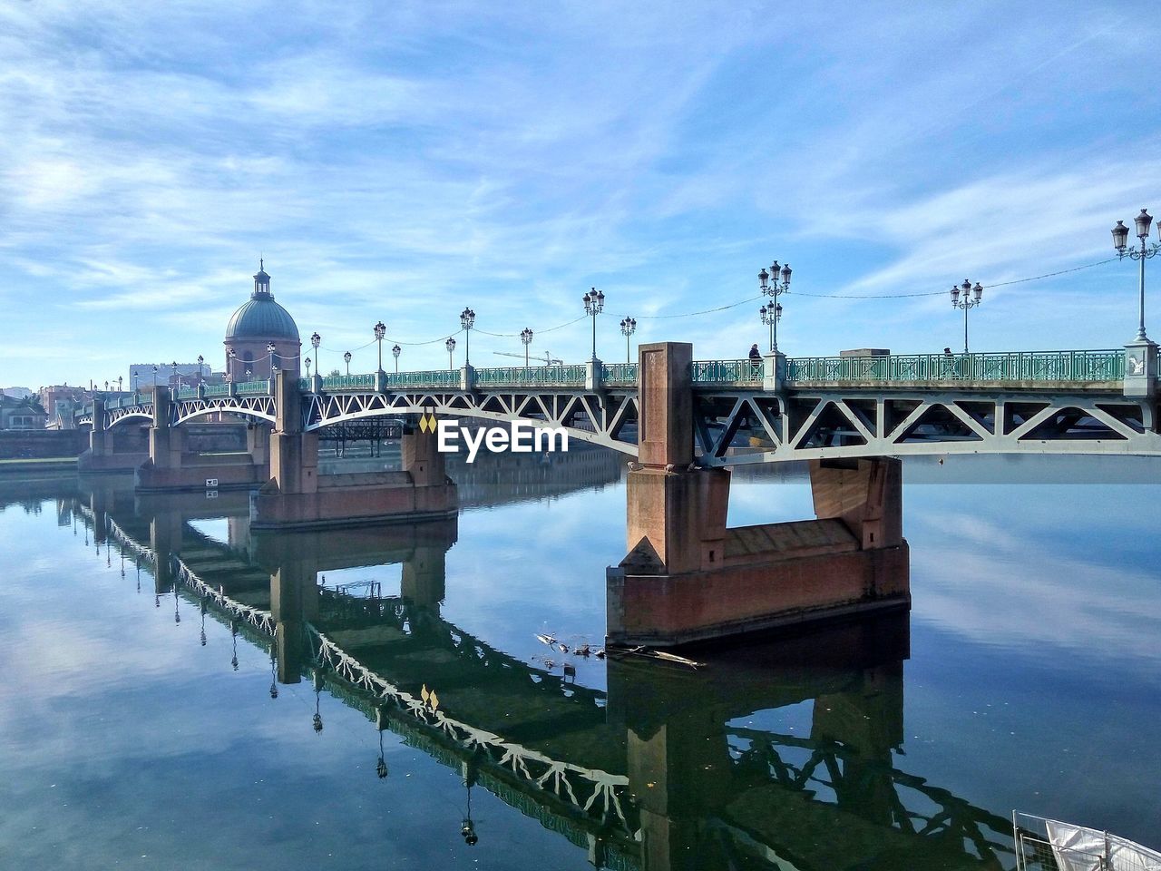 Reflection of bridge over calm river against cloudy sky