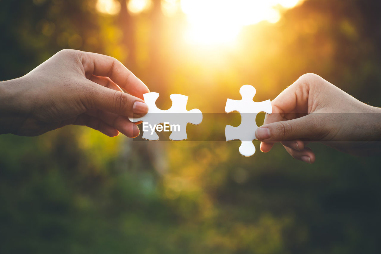 Cropped hands of women holding jigsaw pieces during sunset