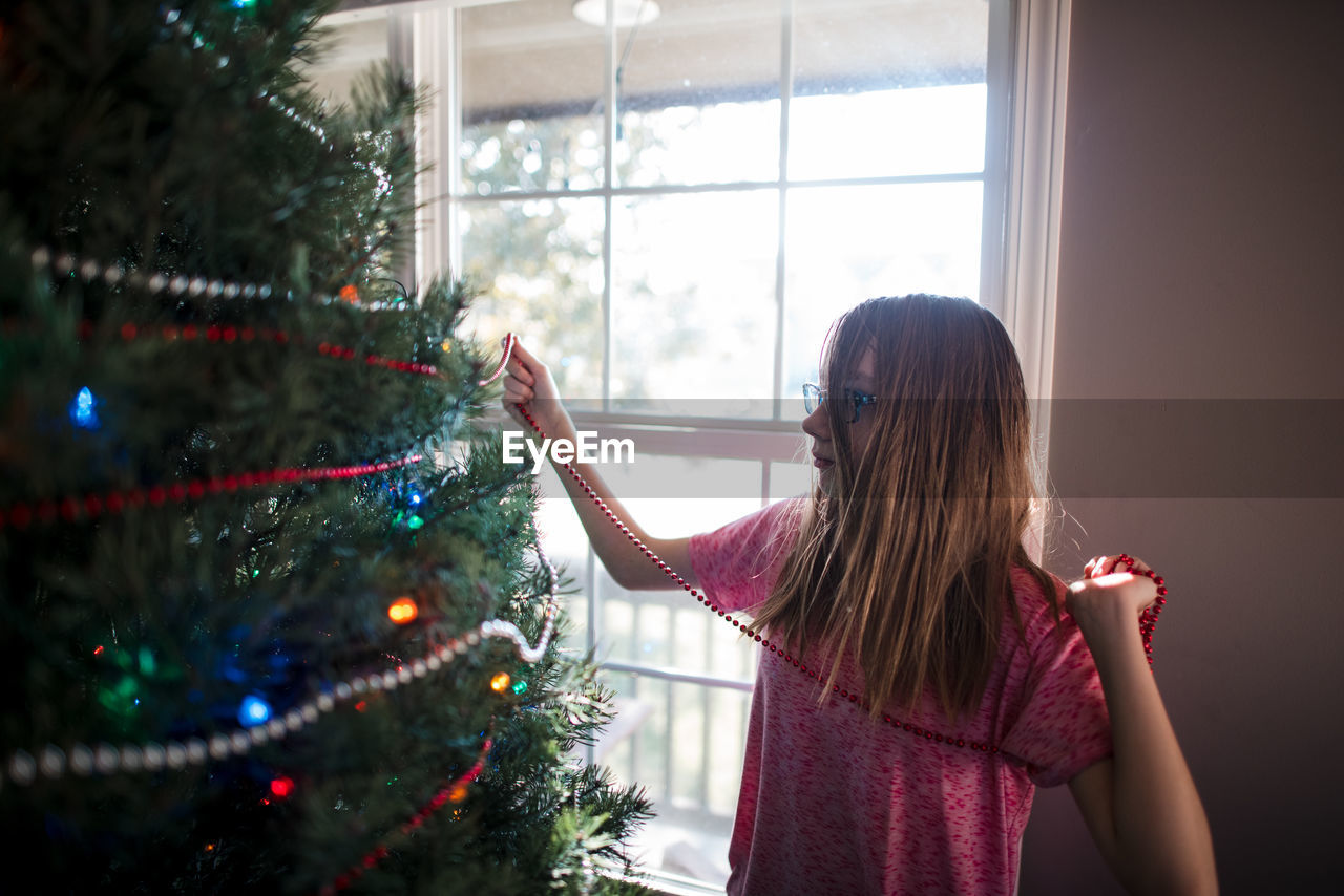 Pre teen girl decorating christmas tree at home