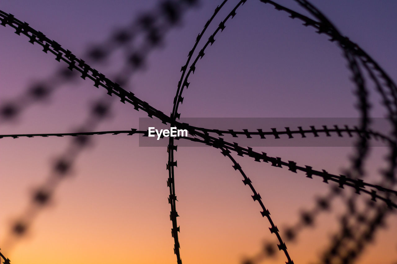 Close-up of barbed wire against sky at sunset