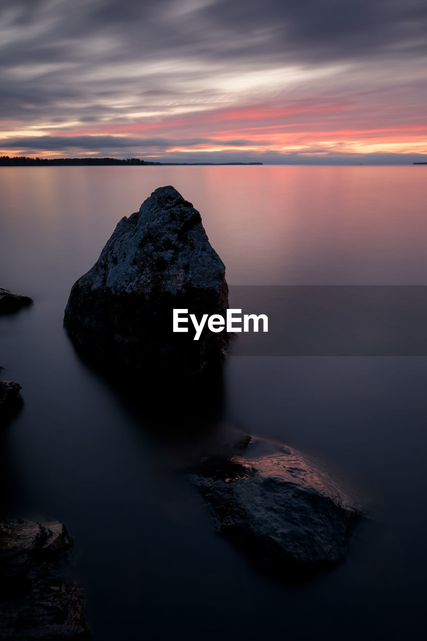 Rocks in sea against sky during sunset