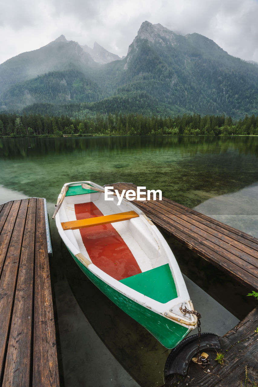 BOATS MOORED ON LAKE AGAINST MOUNTAIN RANGE