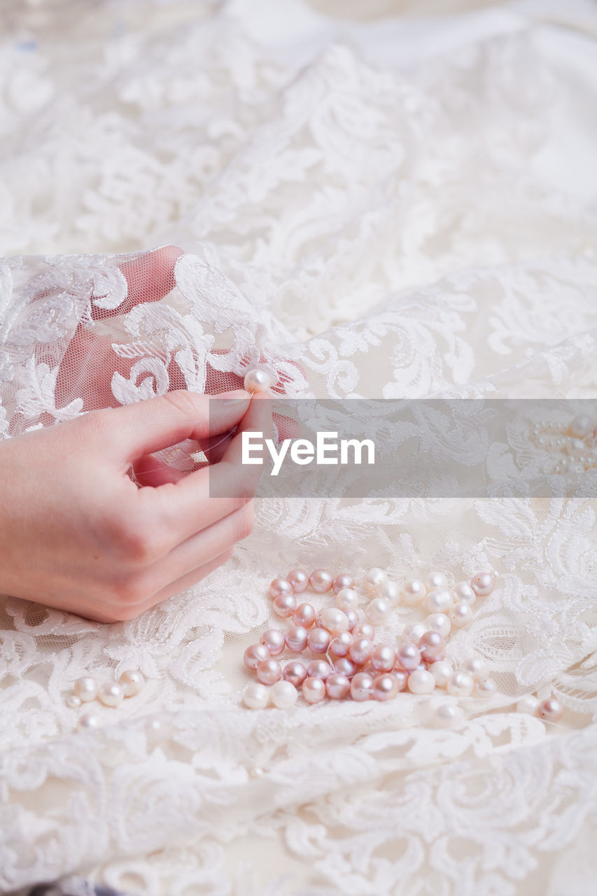 Cropped hand of woman stitching pearls on white wedding dress