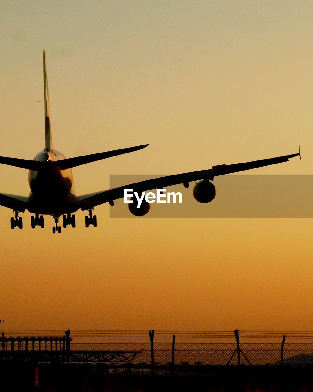 Airplane over airport runway against clear sky during sunset