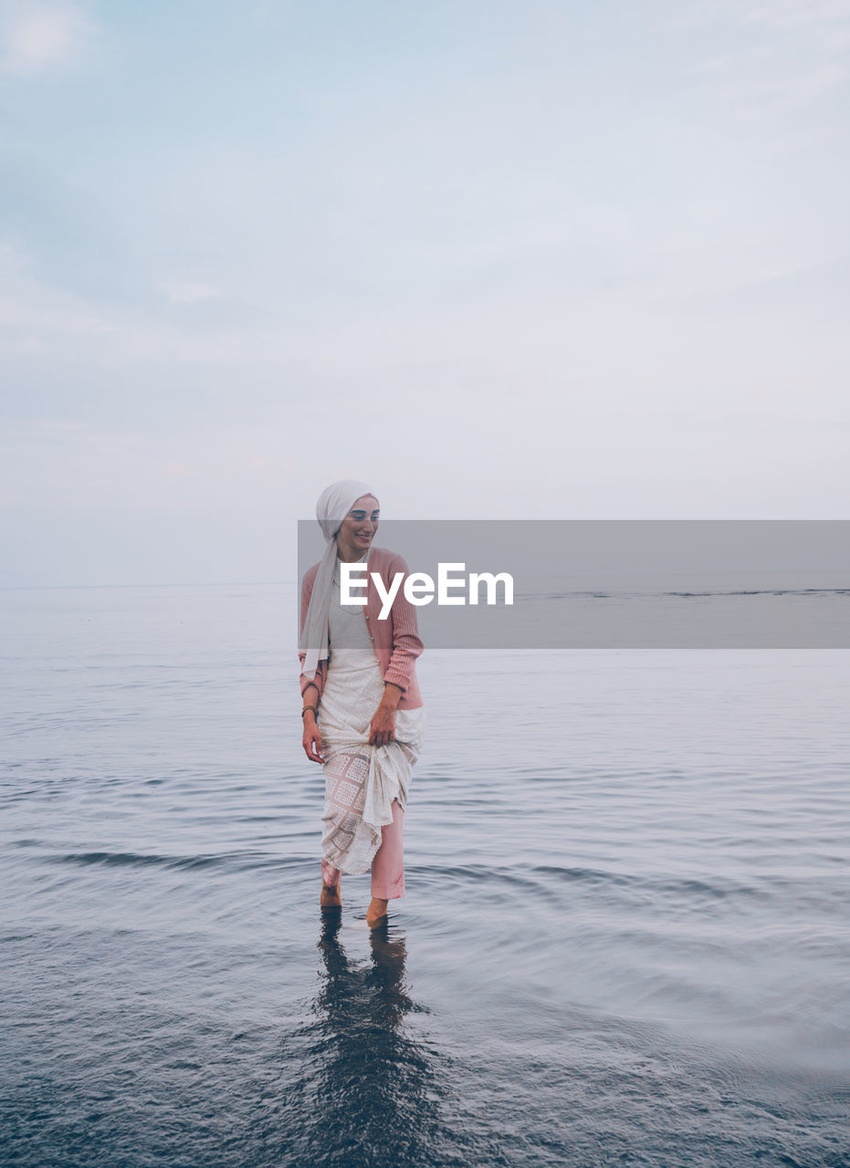 Woman wading in sea against sky