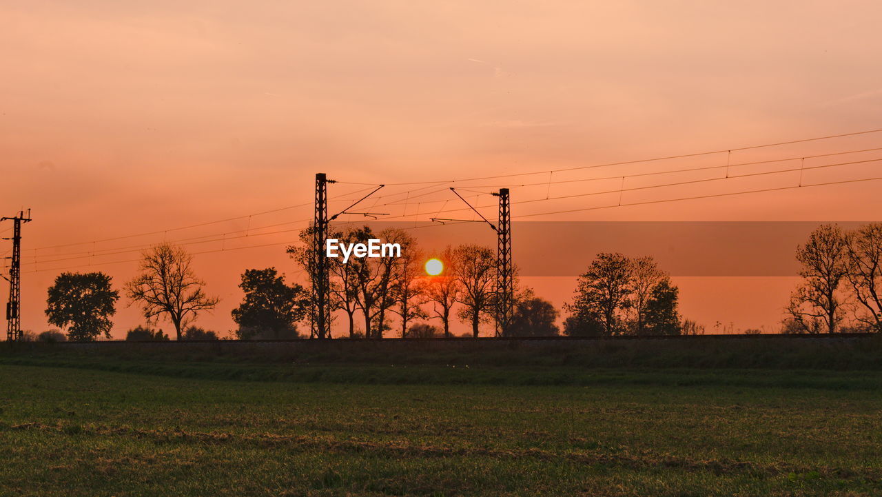 Scenic view of field and railroad against sky during sunset