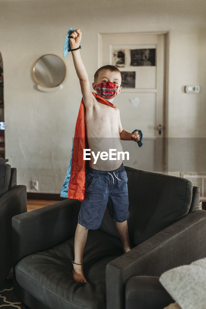 Young boy dressed as super hero standing on couch with mask on