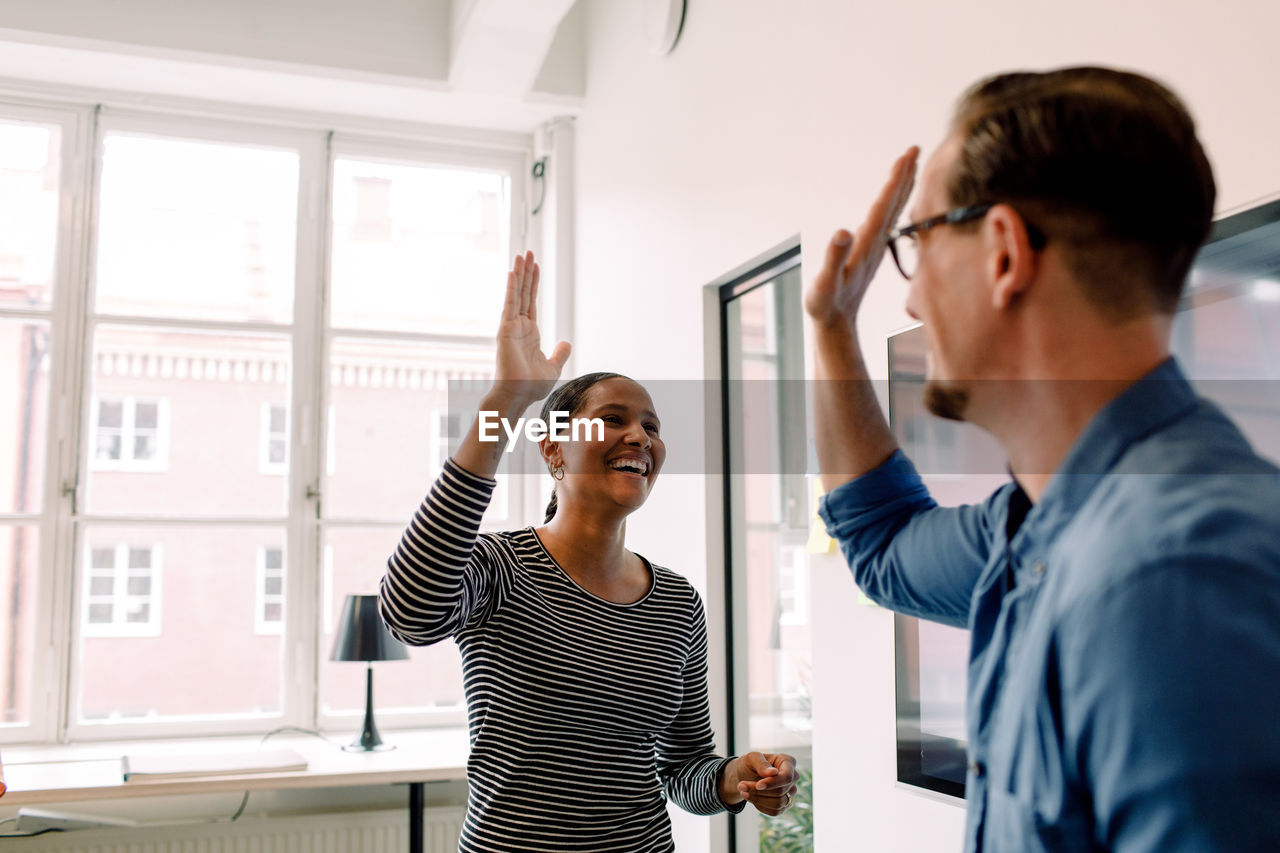 Happy businesswoman giving high-five to male colleague in office