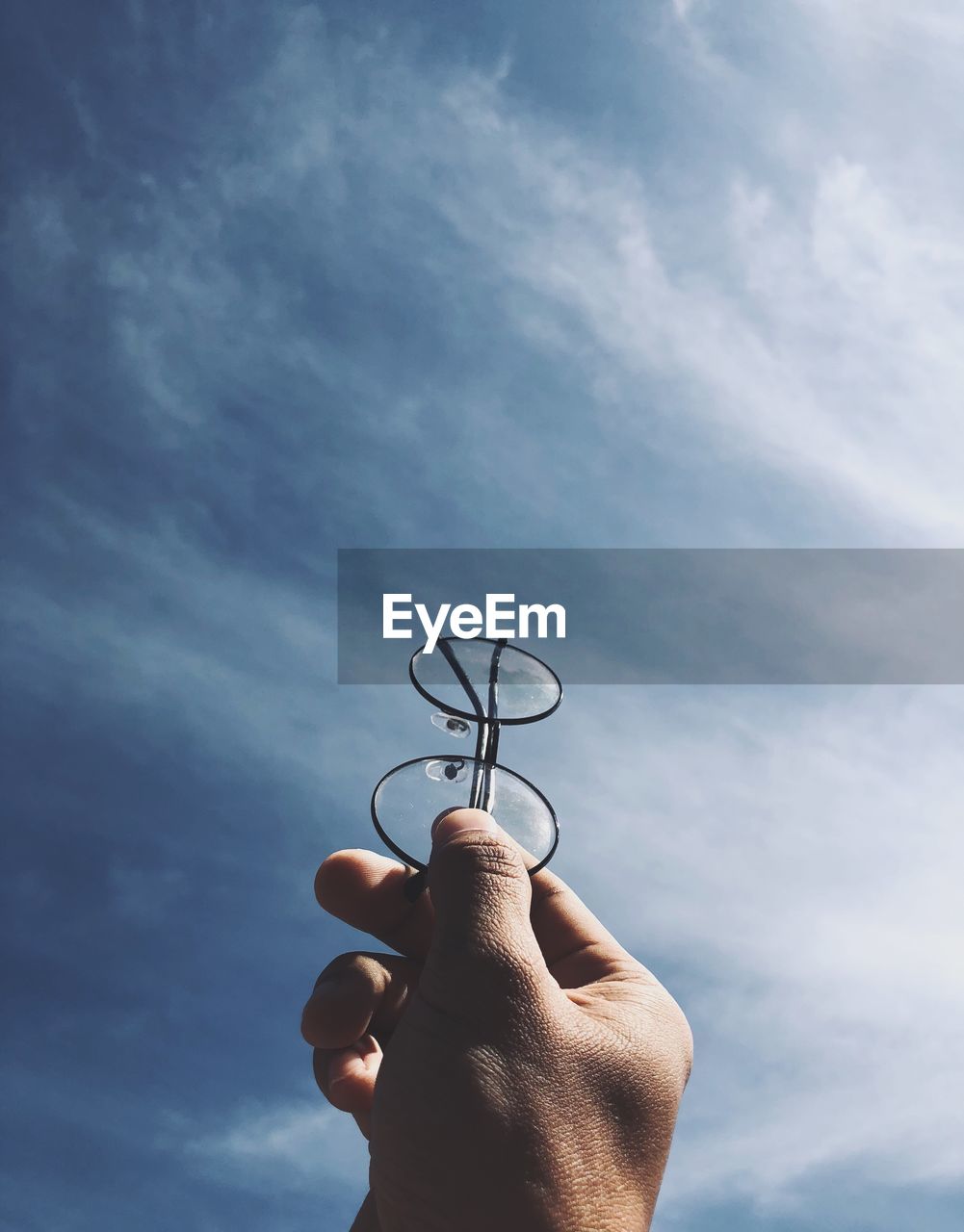 Low angle view of hand holding eyeglasses against sky