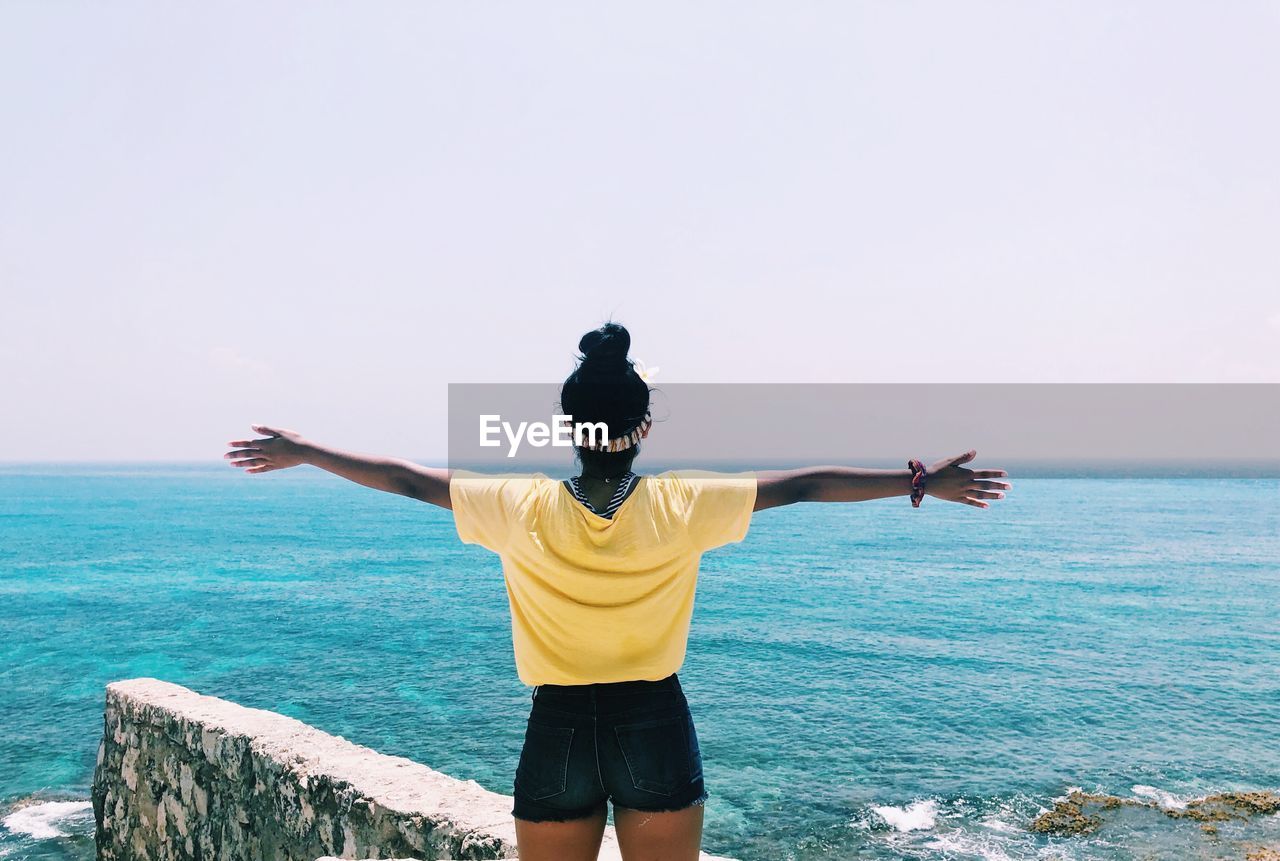 Rear view of woman with arms outstretched looking at sea against sky