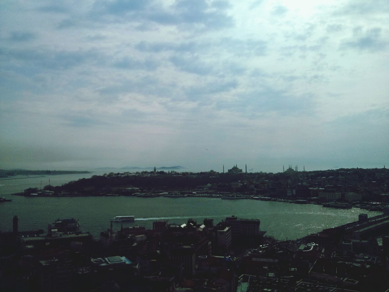 Sea and cityscape against cloudy sky