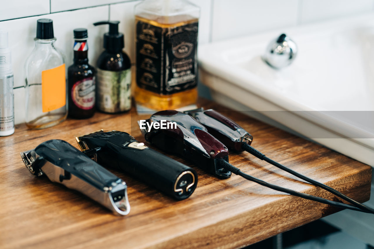 Collection of professional electric clippers near bottles of cosmetic products and washbasin in bathroom of barbershop