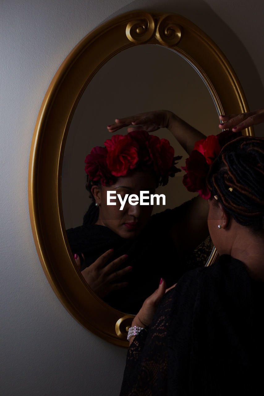 Beautiful woman dressed in black with red flowers on head in from  of a mirror.