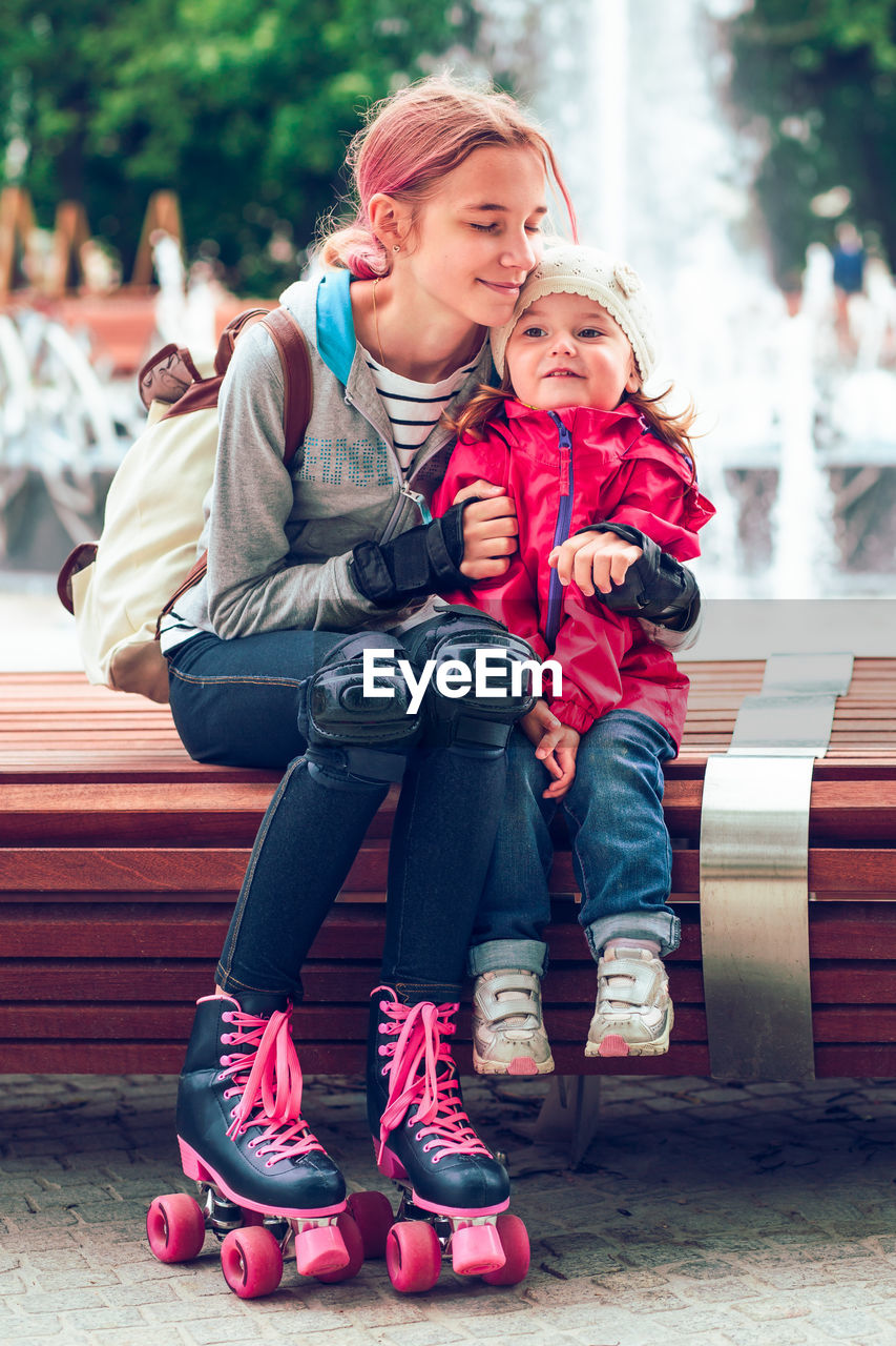 Full length of girl with sister on bench against fountain at park