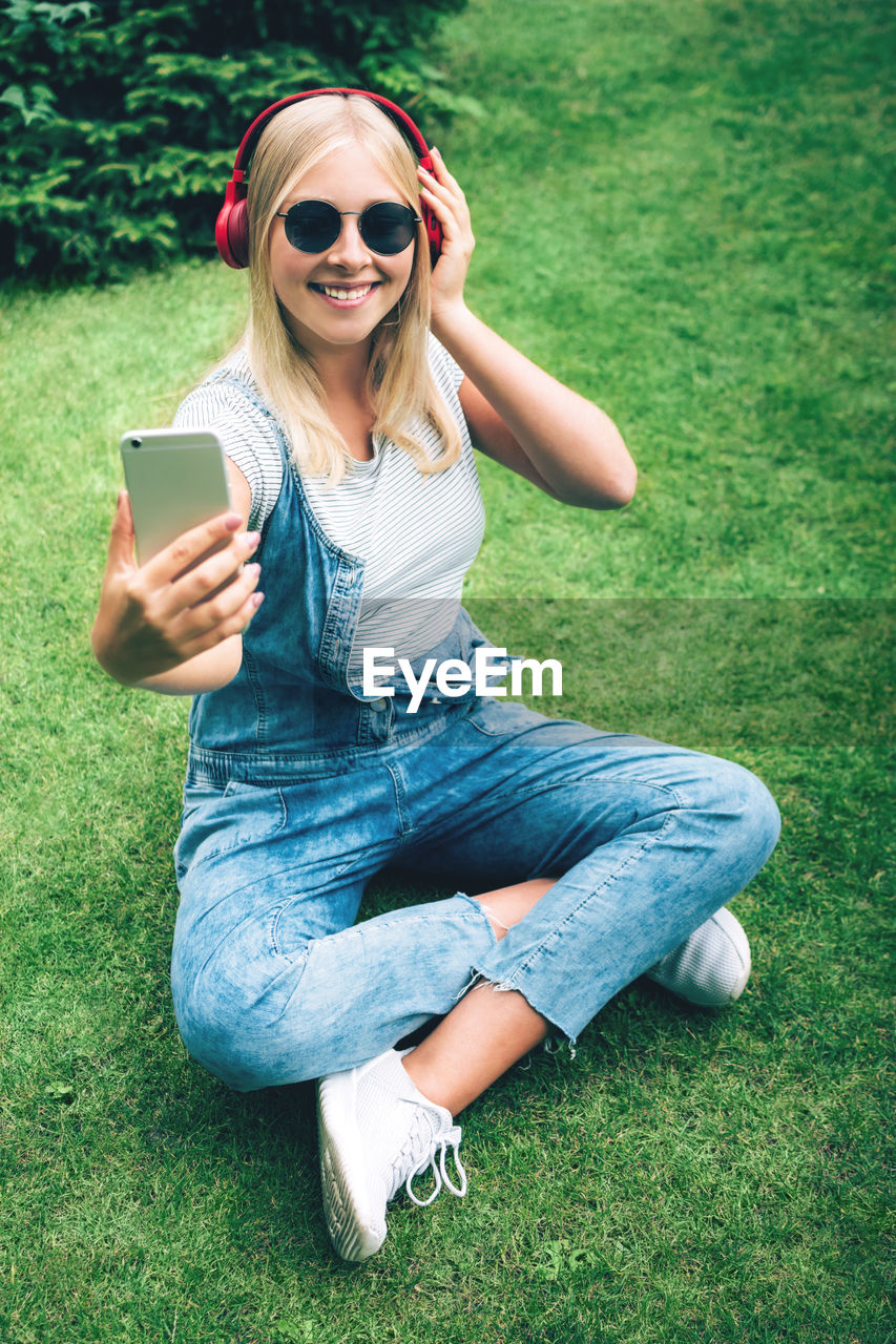 Teenage girl with headphones taking selfies through mobile phone on field