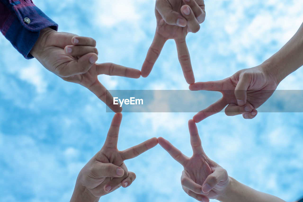 Directly below shot of people making star shape with fingers against sky