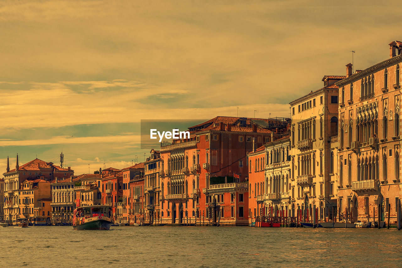 Buildings by canal against sky in city