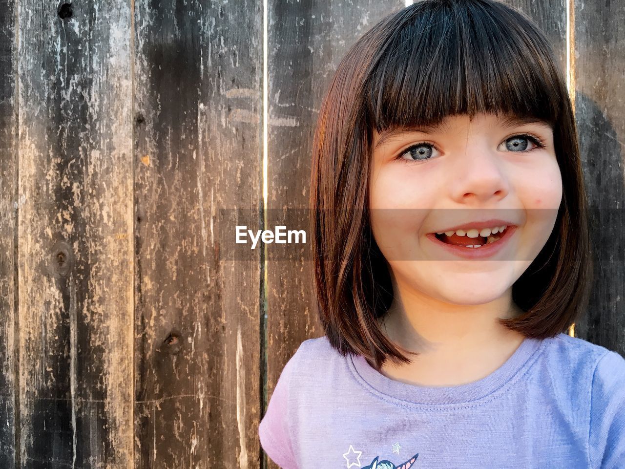 Close-up of happy girl against wooden fence