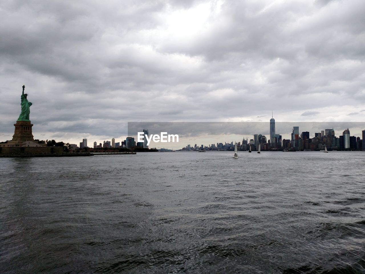 Cityscape by hudson river against cloudy sky