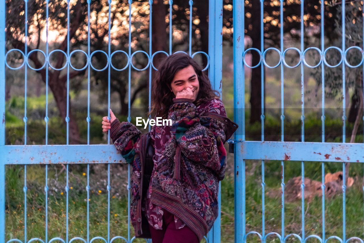 Smiling man with hand covering mouth standing by gate