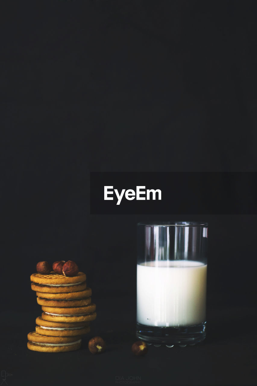 Biscuits by glass of milk against black background