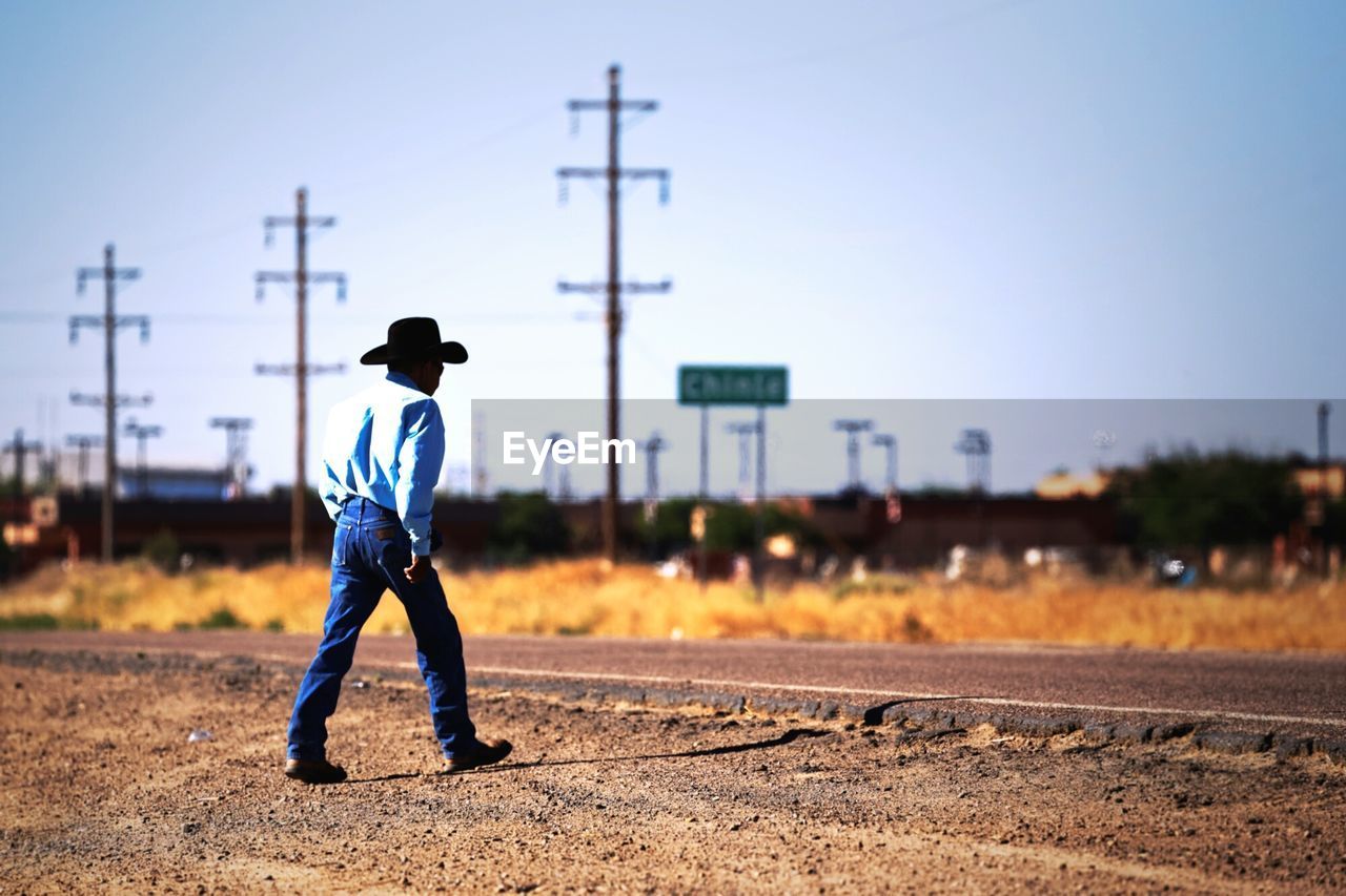Full length of man walking on field by road against clear sky