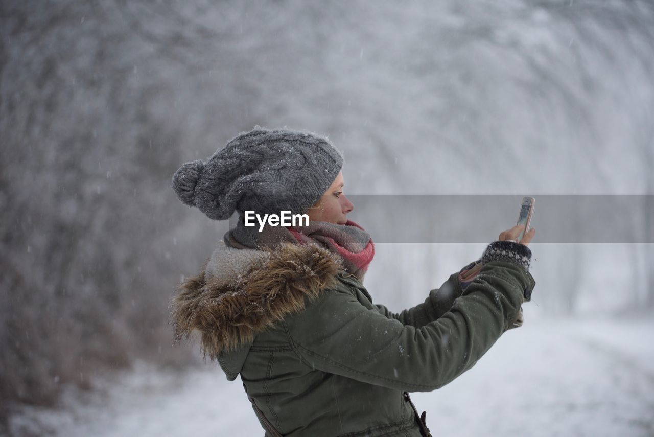 Side view of woman photographing through smart phone during winter