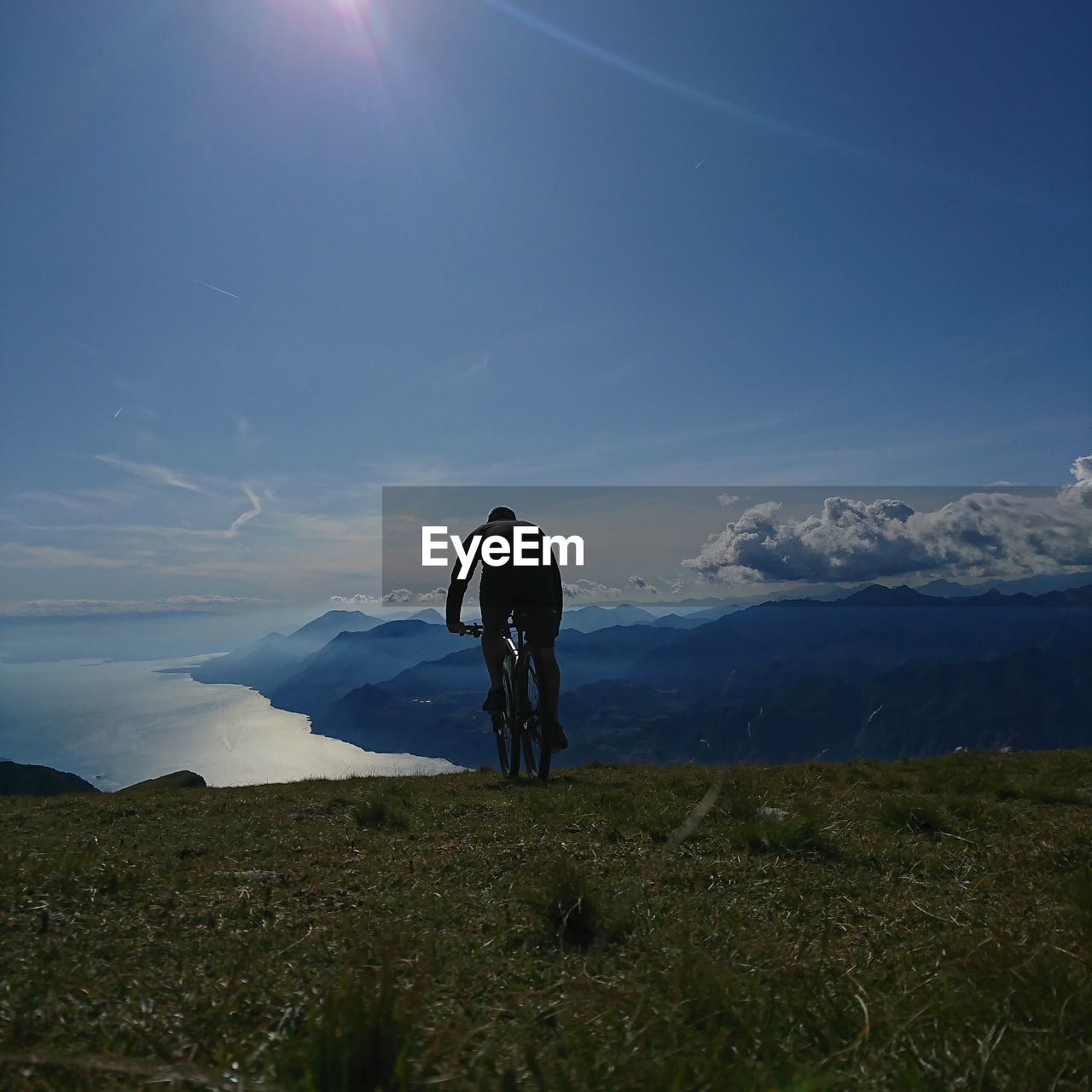 REAR VIEW OF MAN RIDING BICYCLE AGAINST SKY