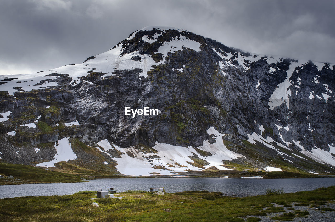 Scenic view of lake and snowcapped mountain against cloudy sky