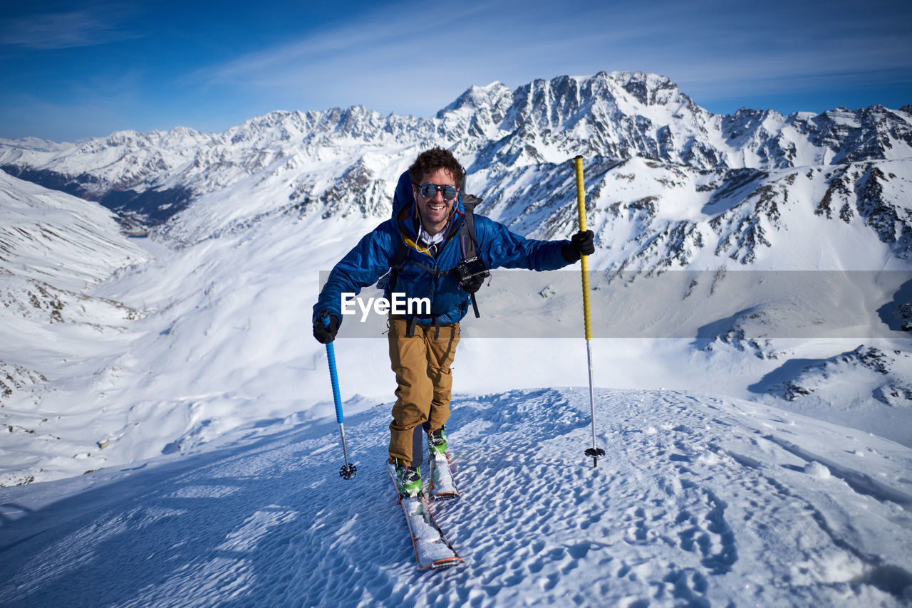 Smiling man ski touring up slope with mountains behind