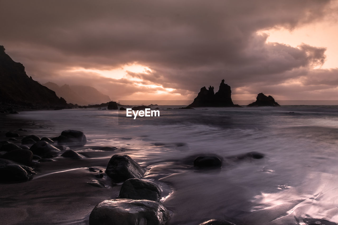 Long exposure of beach onnorth coast of canary island of tenerife at sunset with dramatic clouds .