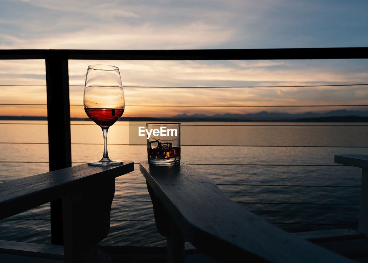 Wine and whiskey on deck chairs at sunset over the sea, landscape.