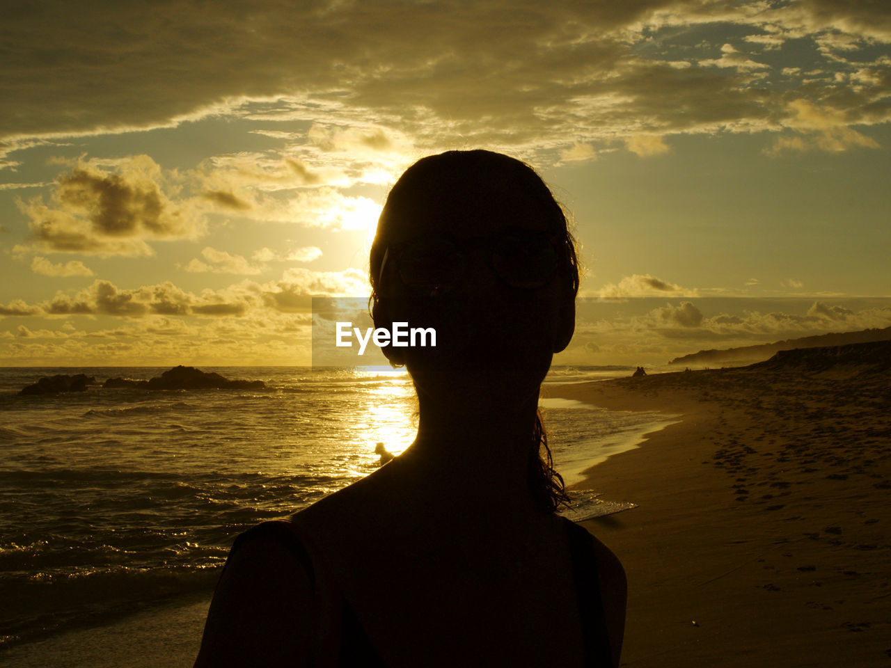 PORTRAIT OF WOMAN ON BEACH AGAINST SUNSET SKY