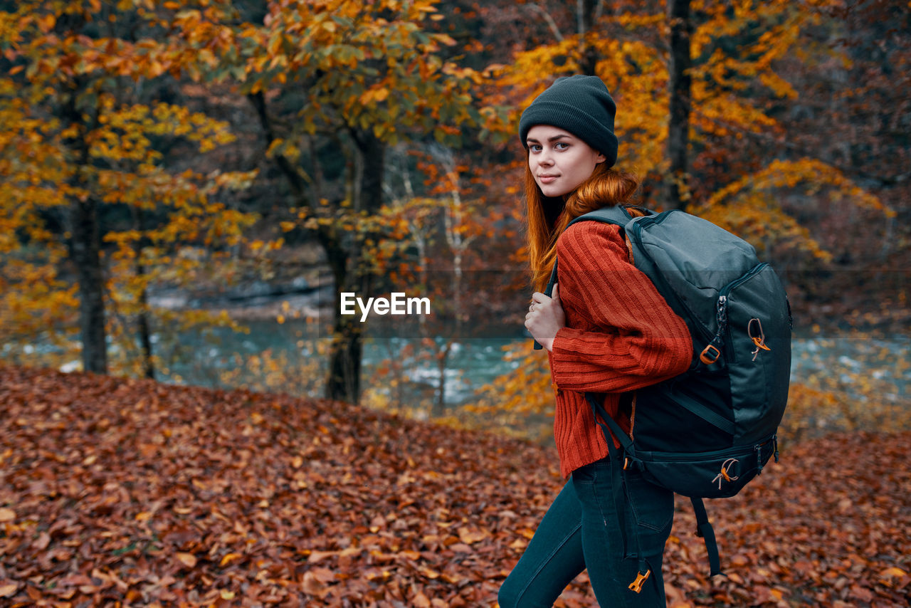 Portrait of young woman standing by autumn leaves