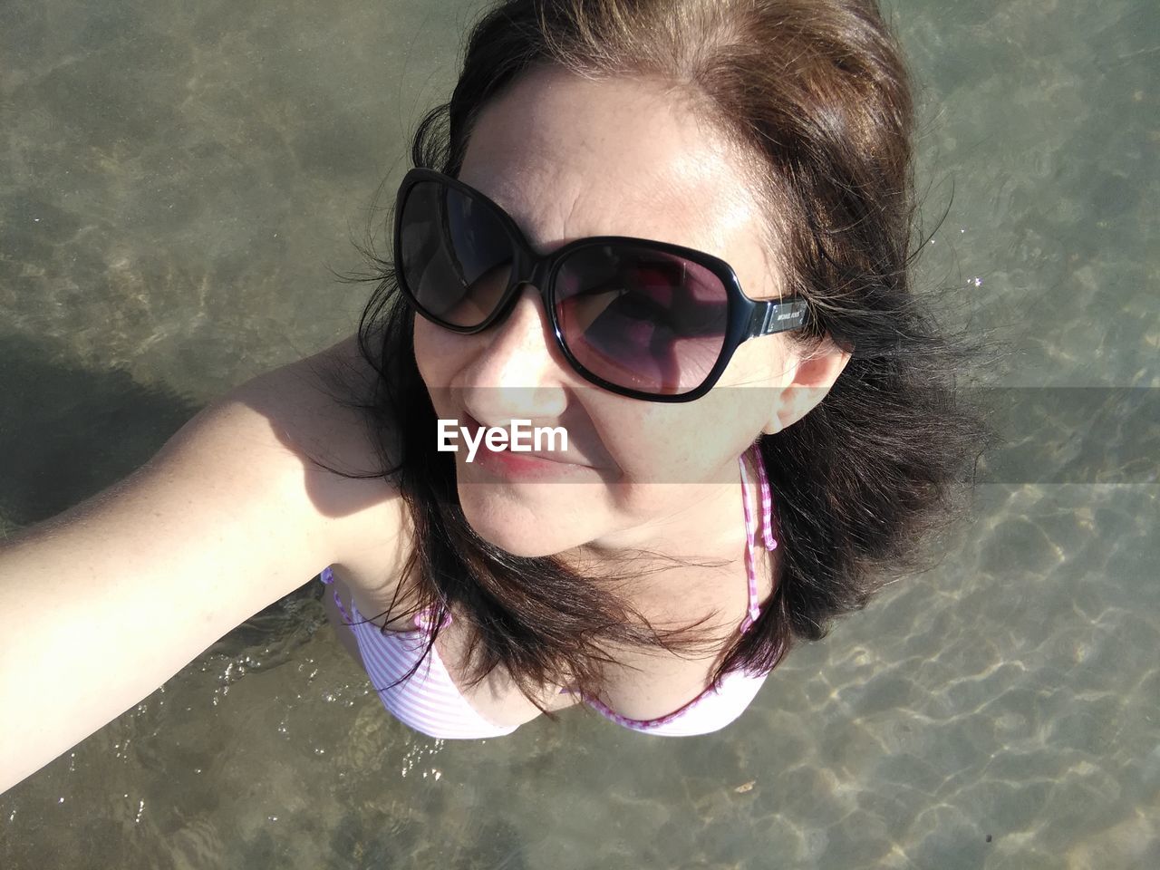 High angle portrait of young woman wearing sunglasses standing at beach