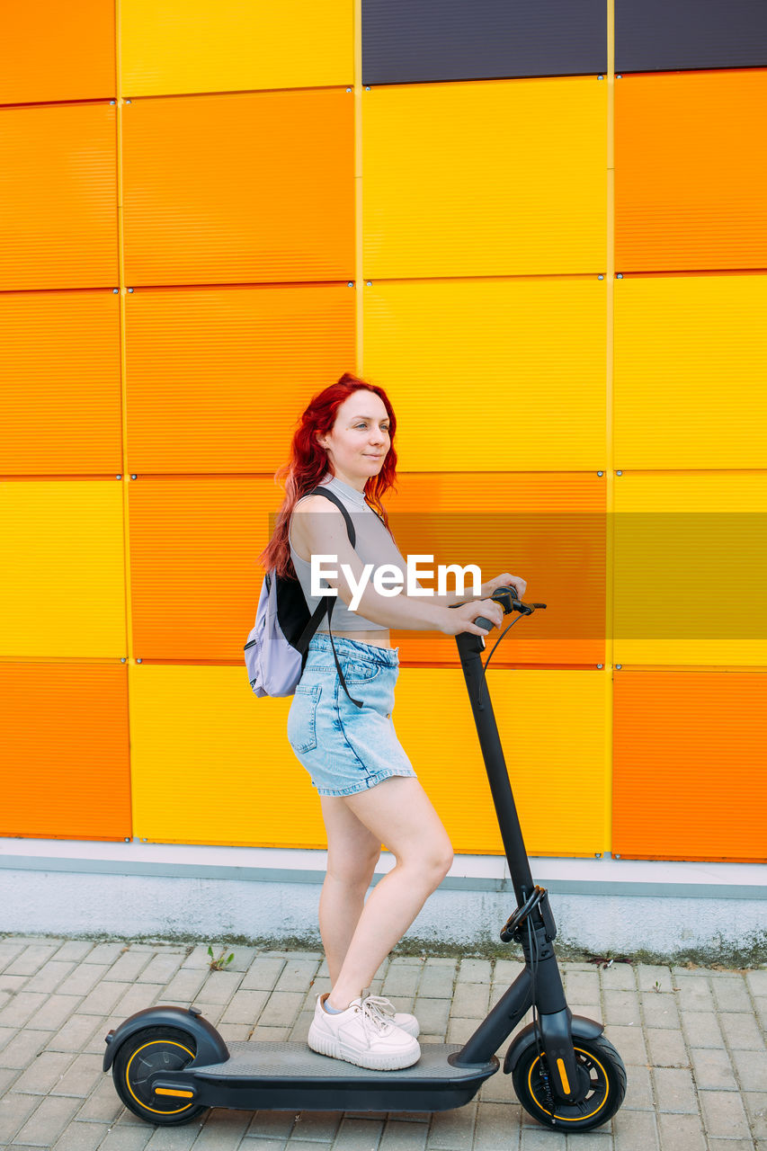 Young bright woman smiles and rides an electric scooter in the summer in city