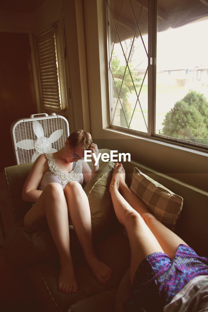 Low section of young woman with sister relaxing on sofa at home