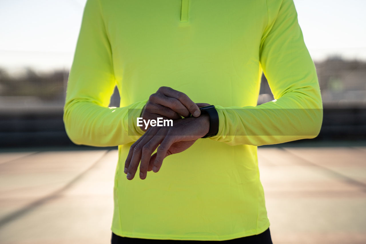 Male athlete checking time at sports court during sunny day