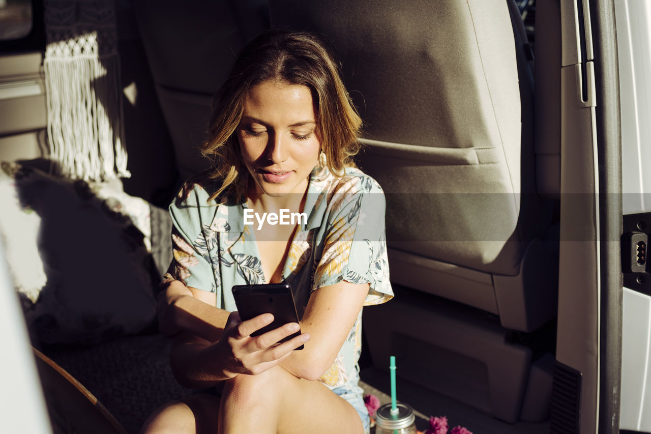 Blonde pretty woman into a minivan using her smartphone with sun getting into van