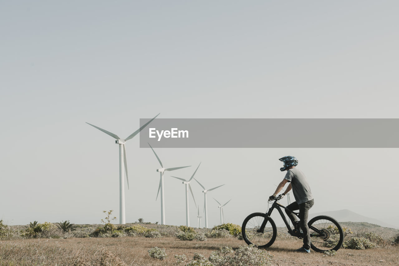 Spain, lanzarote, mountainbiker on a trip in desertic landscape with wind turbines in background