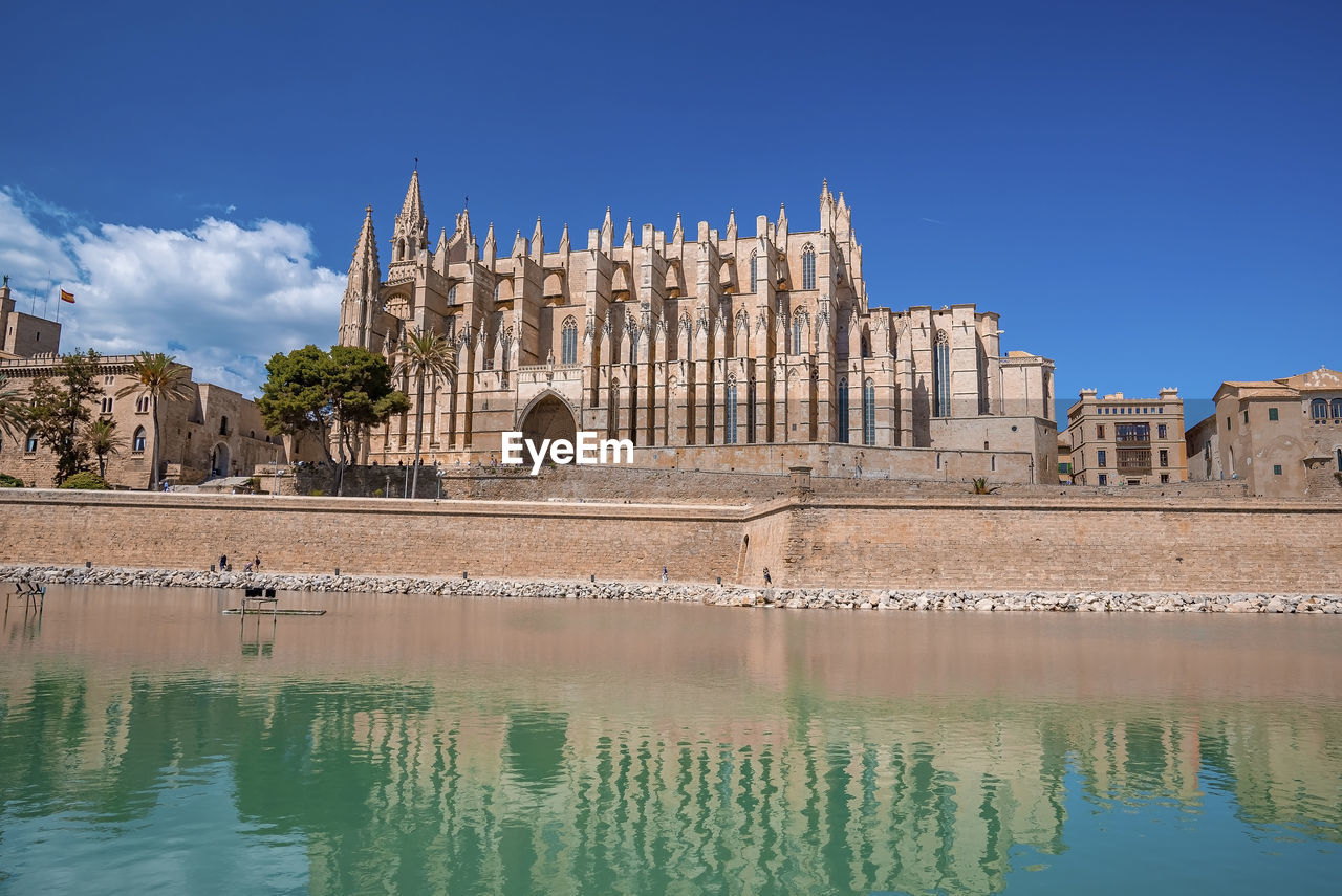 Medieval la seu cathedral reflecting in canal water against blue sky at city