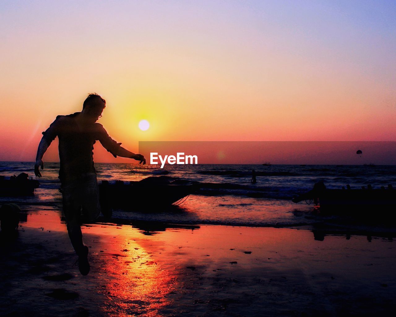 SILHOUETTE MAN STANDING ON BEACH AGAINST ORANGE SUNSET SKY