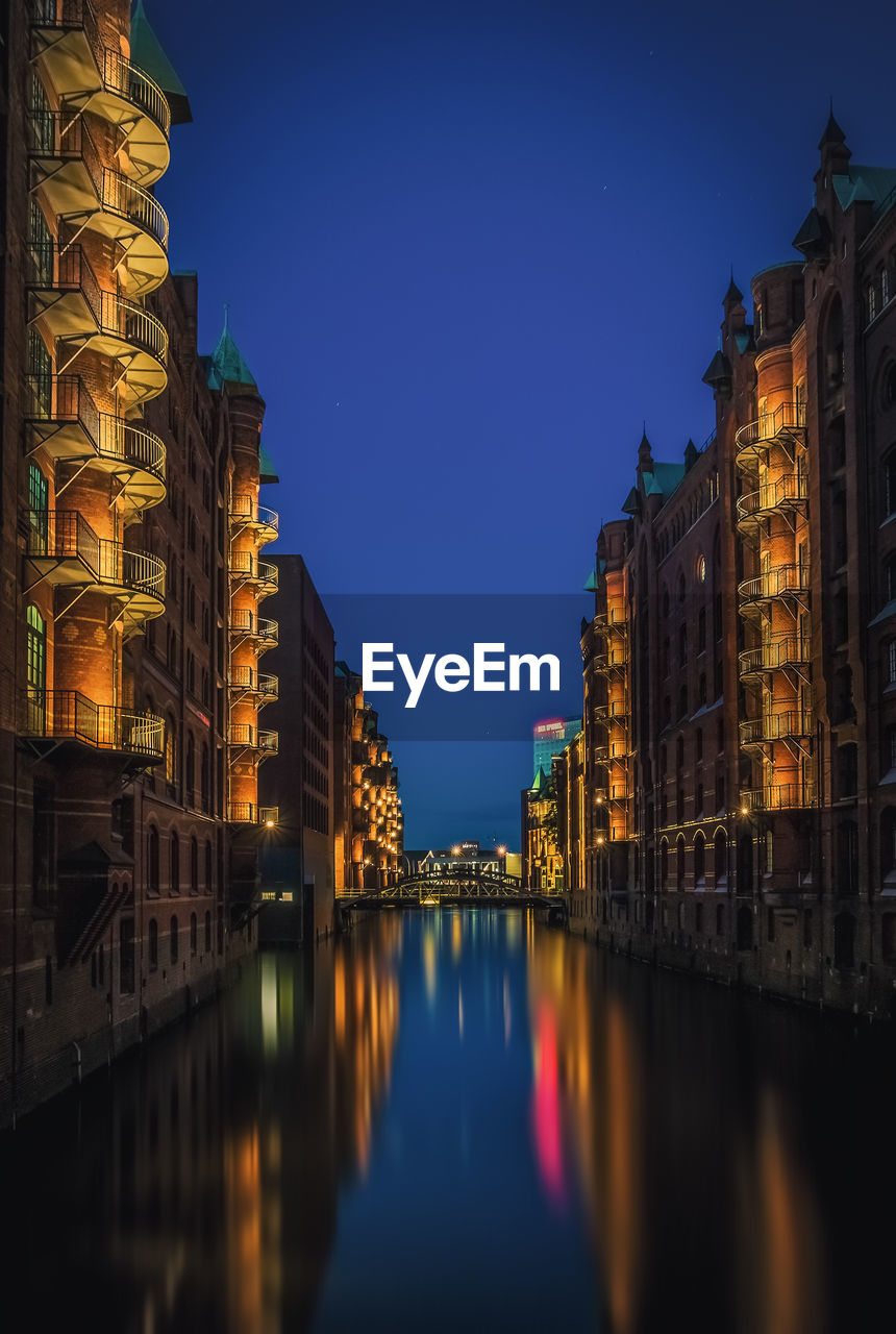 Illuminated buildings by river against sky at night