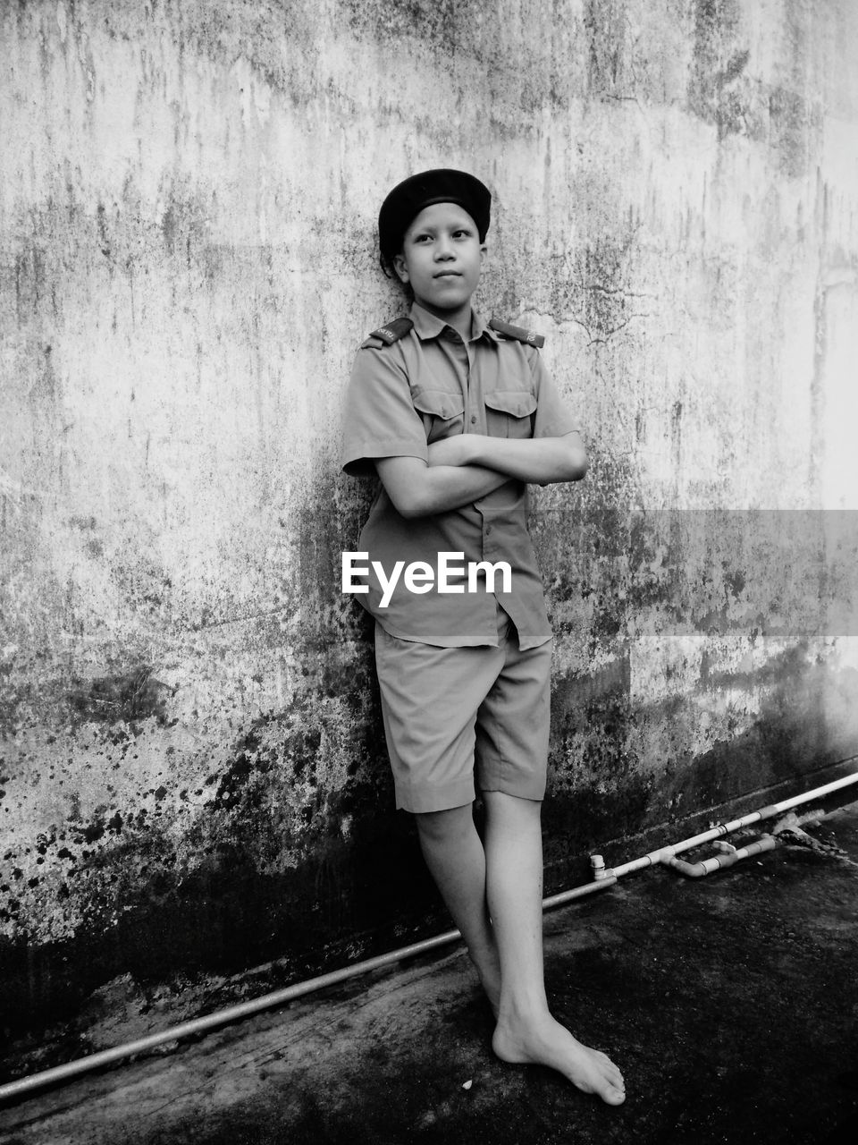 Boy with arms crossed wearing police uniform while standing by weathered wall