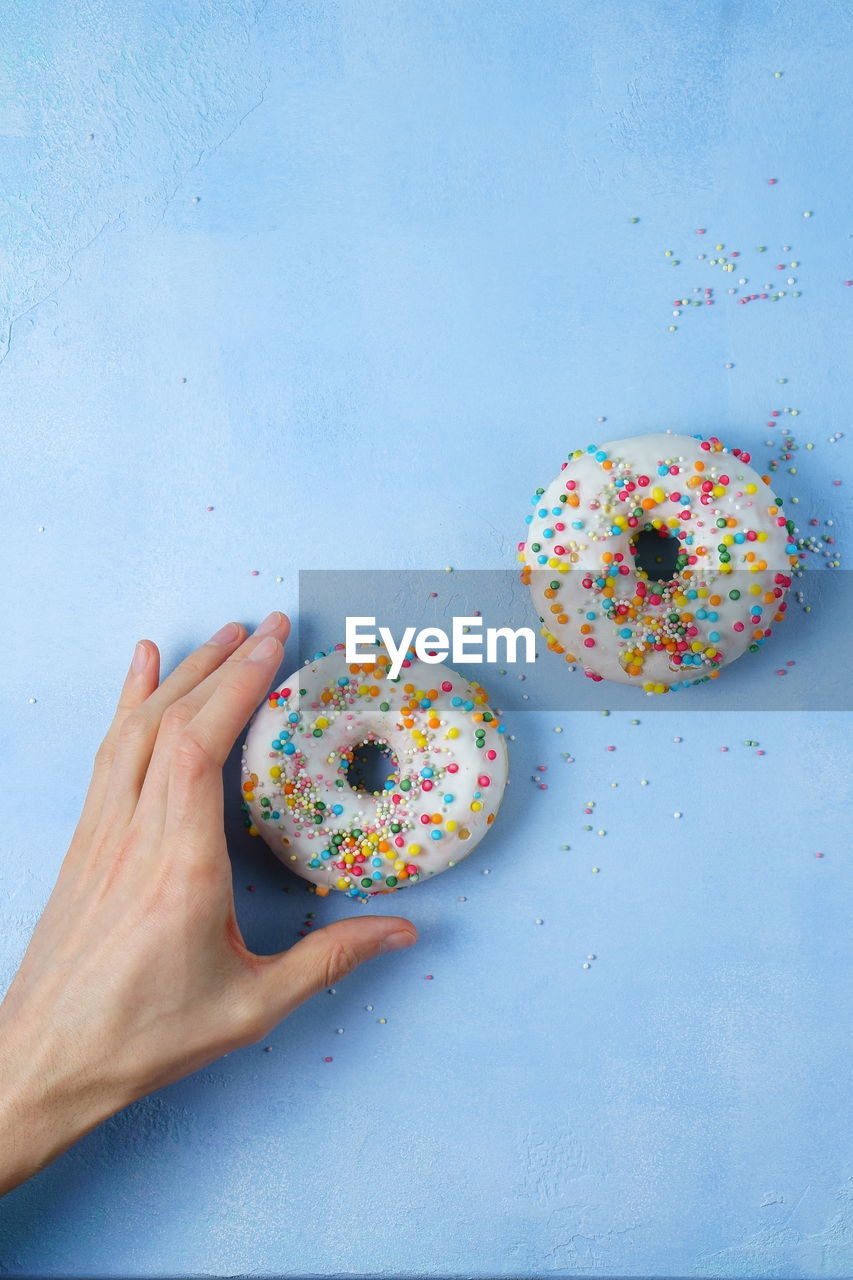 Cropped hand of person reaching for donut on blue background